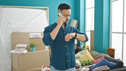 Young hispanic man speaking on the phone looking at the time at new home