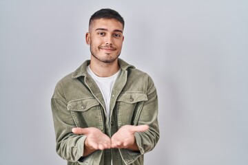 Young hispanic man standing over isolated background smiling with hands palms together receiving or giving gesture. hold and protection