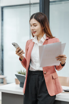 Using mobile smartphone, Excited Asian business woman secretary working with product liability, Scarcity, Negotiate, Proposal, Advertising Cost & How to Buy Ads on Any Budget, Interest rate, Dividend