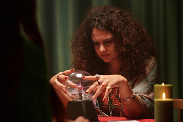 Frowning fortune teller looking into crystal ball, predicting future of woman