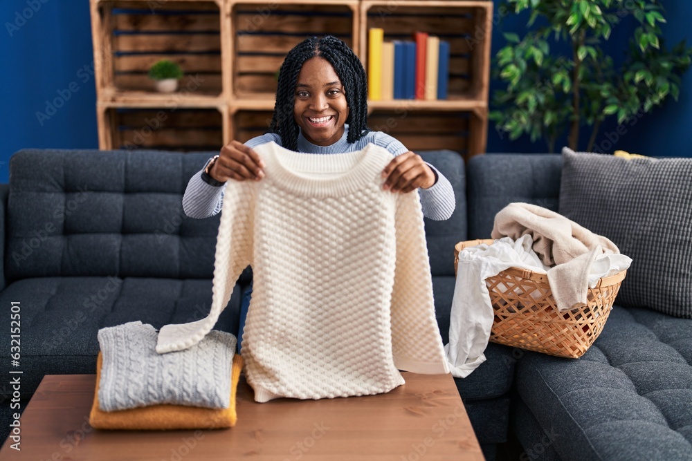 Wall mural African american woman folding clean laundry smiling and laughing hard out loud because funny crazy joke.