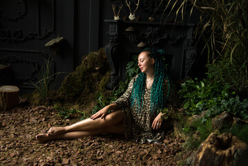 portrait of a beautiful woman with green hair and blue eyes with sitting in green leaves in dark studio