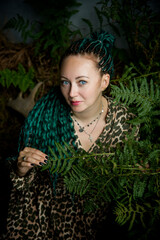 portrait of a beautiful woman with green hair and blue eyes with green leaves in dark studio