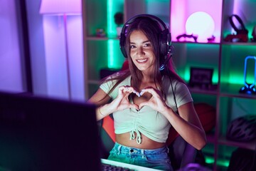 Young beautiful hispanic woman streamer smiling confident doing heart symbol with hands at gaming room