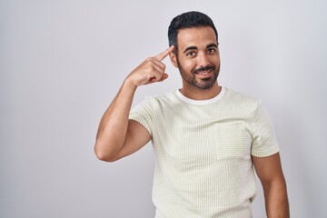 Fototapeta premium Hispanic man with beard standing over isolated background smiling pointing to head with one finger, great idea or thought, good memory