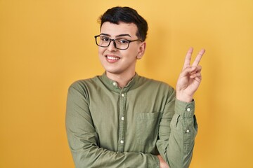 Non binary person standing over yellow background smiling with happy face winking at the camera...
