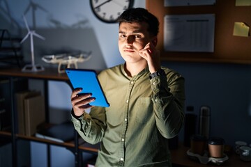 Non binary person using touchpad device at night mouth and lips shut as zip with fingers. secret...