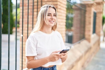 Fototapeta premium Young blonde woman smiling confident using smartphone at street