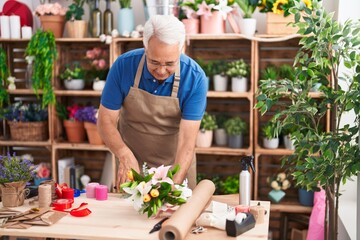 Middle age grey-haired man florist make bouquet of flowers at florist