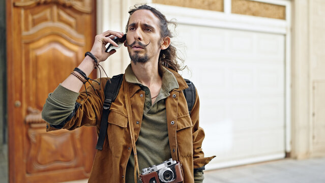 Young hispanic man tourist talking on smartphone looking upset at street