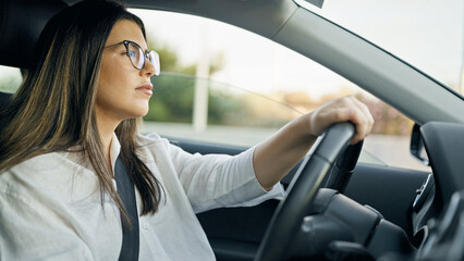 Fototapeta na wymiar Young beautiful hispanic woman driving a car wearing glasses on the road