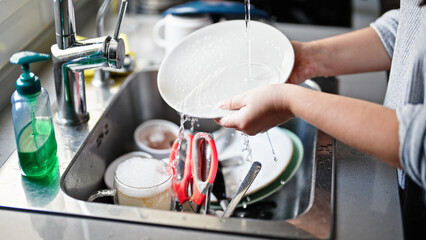 Young beautiful hispanic woman washing plates at the kitchen
