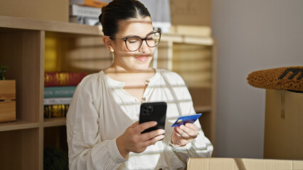 Young beautiful hispanic woman using smartphone and credit card at home