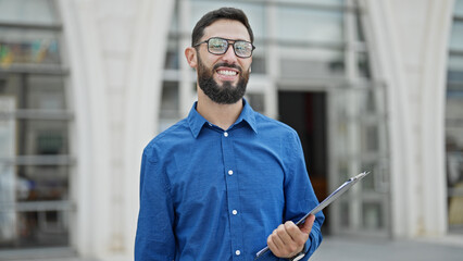 Young hispanic man business worker smiling confident holding clipboard at street