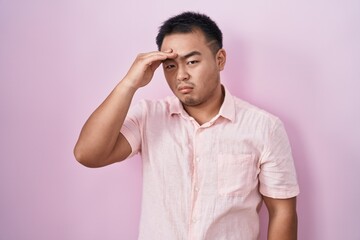 Chinese young man standing over pink background worried and stressed about a problem with hand on forehead, nervous and anxious for crisis