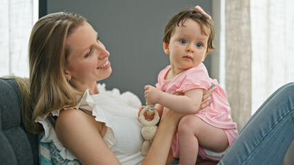 Mother and daughter hugging each other sitting on sofa at home