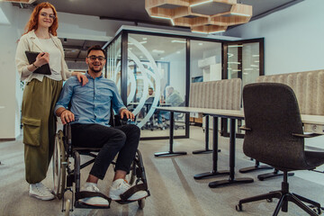 Fototapeta na wymiar Young business colleagues, collaborative business colleagues, including a person in a wheelchair, walk past a modern glass office corridor, illustrating diversity, teamwork and empowerment in the
