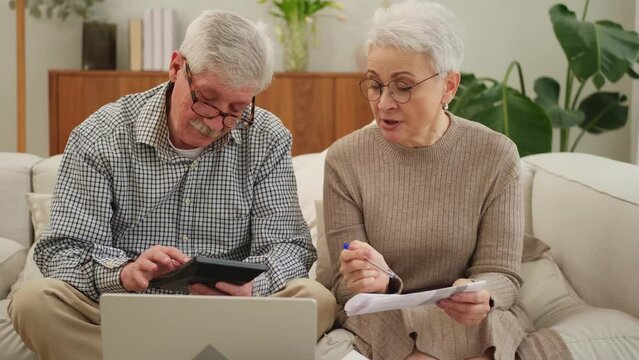 Middle aged senior couple sit with laptop and paper document. Older mature man woman reading paper bill pay online at home managing bank finances calculating taxes planning loan debt pension payment