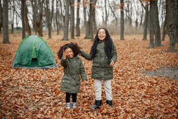 Naklejka premium Two little black sisters playing near tent camping in the autumn forest