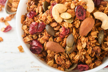 Homemade granola in glass jar with greek yogurt or milk and cashews, almonds, pumpkin with dried cranberry seeds in on white rustic wooden table background. Healthy energy breakfast or snack. Top view