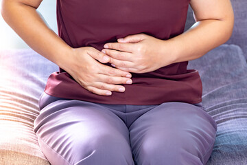 Fat woman having painful stomach ache. eating on time due to wanting to control weight on sofa in the living room, Chronic gastritis. Stomach or menstrual cramps. Health problem Inflammation in body