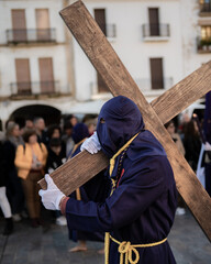Caceres. Spain. April 2, 2023: Person in purple robe and hood carrying a large wooden cross on...