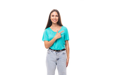 young well-groomed caucasian brunette woman with long hair in a blue t-shirt points her hand to the side on an isolated white background with copy space