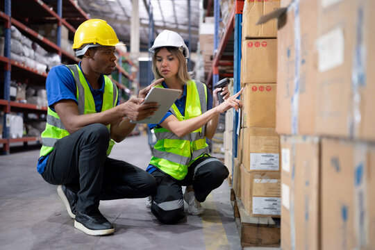 Warehouse worker scanning cardboard boxes on shelf with bar code reader technology. Diverse ethnic people working on inventory checklist using scanner at storage compartment in logistics distribution.