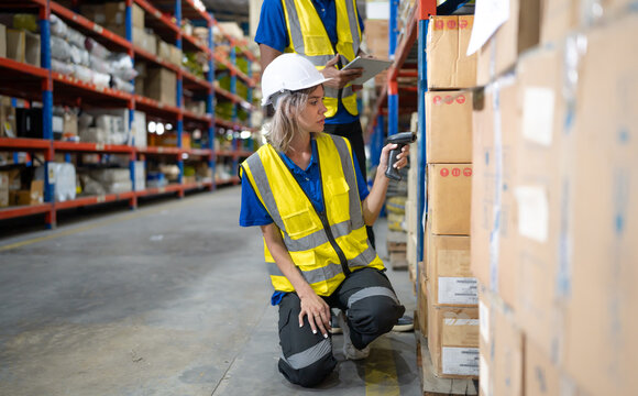 Warehouse worker scanning cardboard boxes on shelf with bar code reader technology. Diverse ethnic people working on inventory checklist using scanner at storage compartment in logistics distribution.