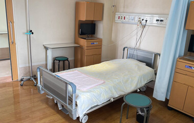A multi-bed hospital room with an empty bed ready for a new patient with a cabinet, TV, and hospital equipment in a Japanese hospital. 