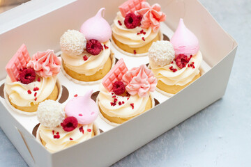 Gift box with beautiful pink cupcakes decorated with mini chocolate bars, meringue, raspberry and cream cheese frosting