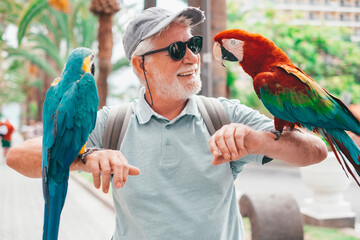 Portrait of smiling bearded senior man with two domestic ara parrots in the park