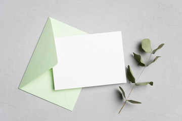 Blank wedding invitation card mockup with envelope and natural eucalyptus twig, flat lay with copy space