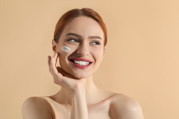 Beautiful young woman with sun protection cream on her face against beige background, space for text