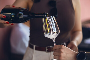 close up shot of female sommelier pouring sparkling wine to guest on outdoor. Restaurant service concept.