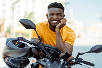 Smiling confident african american man, biker holding helmet and looking at camera