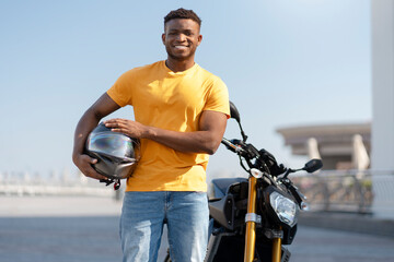 Smiling confident african american man, biker holding helmet and looking at camera