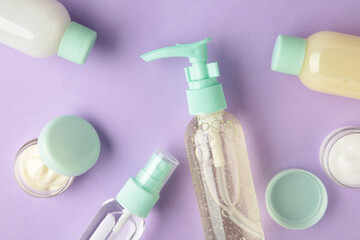 Travel cosmetic bottles on purple background. Minimalist bodycare beauty products for vacation or journey. Top view. Copyspace.