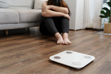 Fototapeta premium Sad woman with fat upset bored of dieting Weight loss fail&nbsp; Fat diet and scale sad asian woman on weight scale at home weight control