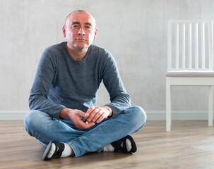 Portrait of confident middle-aged man in casual clothes sitting on the floor in living room