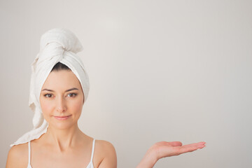 photo of a young pretty woman in white underwear with a white towel smiling, holding something in her hand and looking at the camera.Space for copying.Demonstration and advertising of beauty products