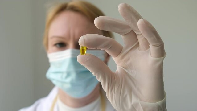 Close up hand of female doctor in white gloves holding yellow transparent omega 3 capsule in hospital or laboratory. Healthcare, medical and pharmacy industry concept