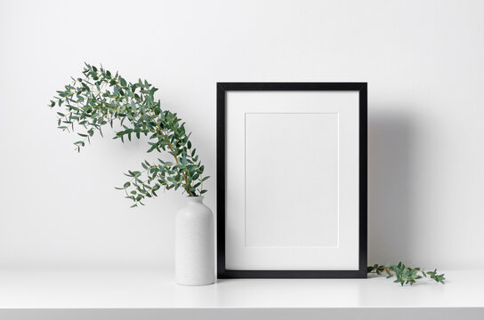 Portrait blank frame mockup in white interior with eucalyptus plant decoration