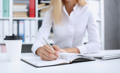 Female hand holding silver pen ready to make note in opened notebook sheet. Businesswoman coffee cup workspace make thoughts records at personal organizer white letter collar conference signature