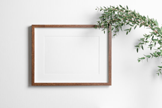 Landscape art frame mockup on white wall with fresh eucalyptus. Blank mock up with copy space for painting or photo design