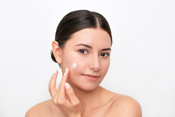 Obraz na płótnie Canvas A young pretty dark-haired Caucasian woman applying a cream on her face and moisturizing skin. Isolated on a white background