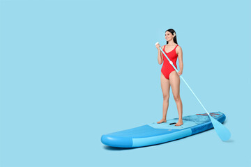 Happy woman with paddle on SUP board against light blue background, space for text