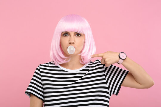 Beautiful woman blowing bubble gum and pointing at herself on pink background