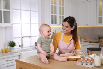 Obraz na płótnie Canvas Happy young woman and her cute little baby cooking together in kitchen