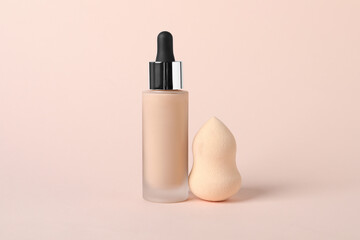 Bottle of skin foundation and sponge on beige background. Makeup product